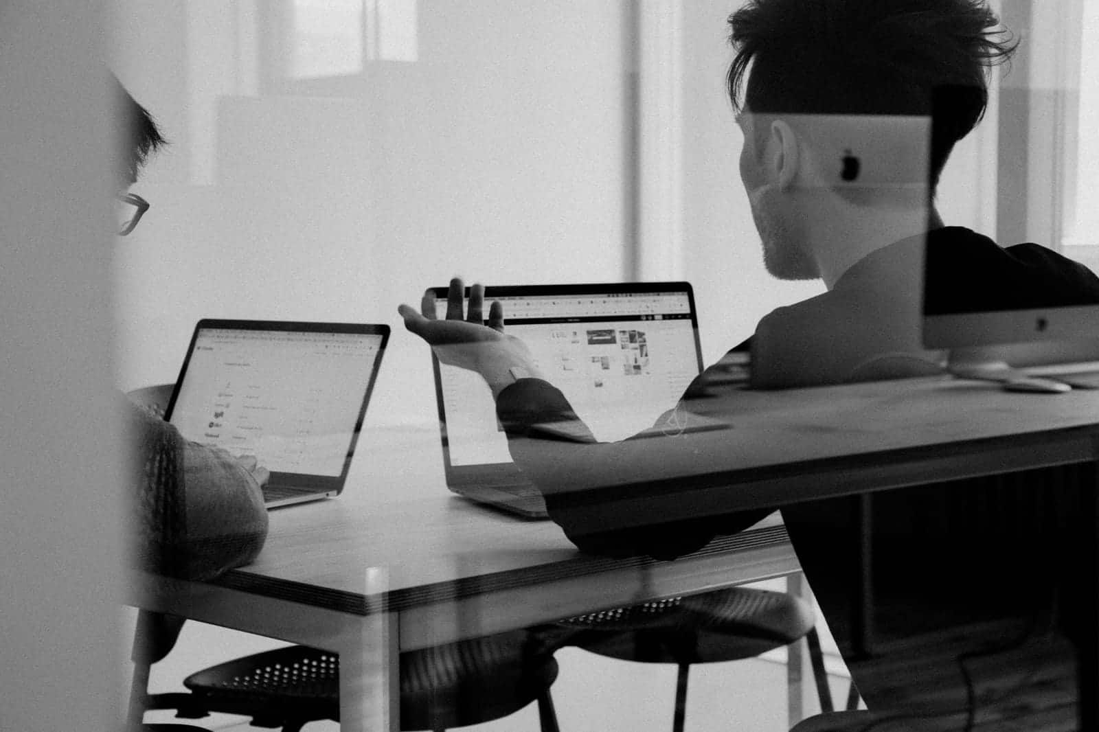 Two people in discussion over laptops, in black and white