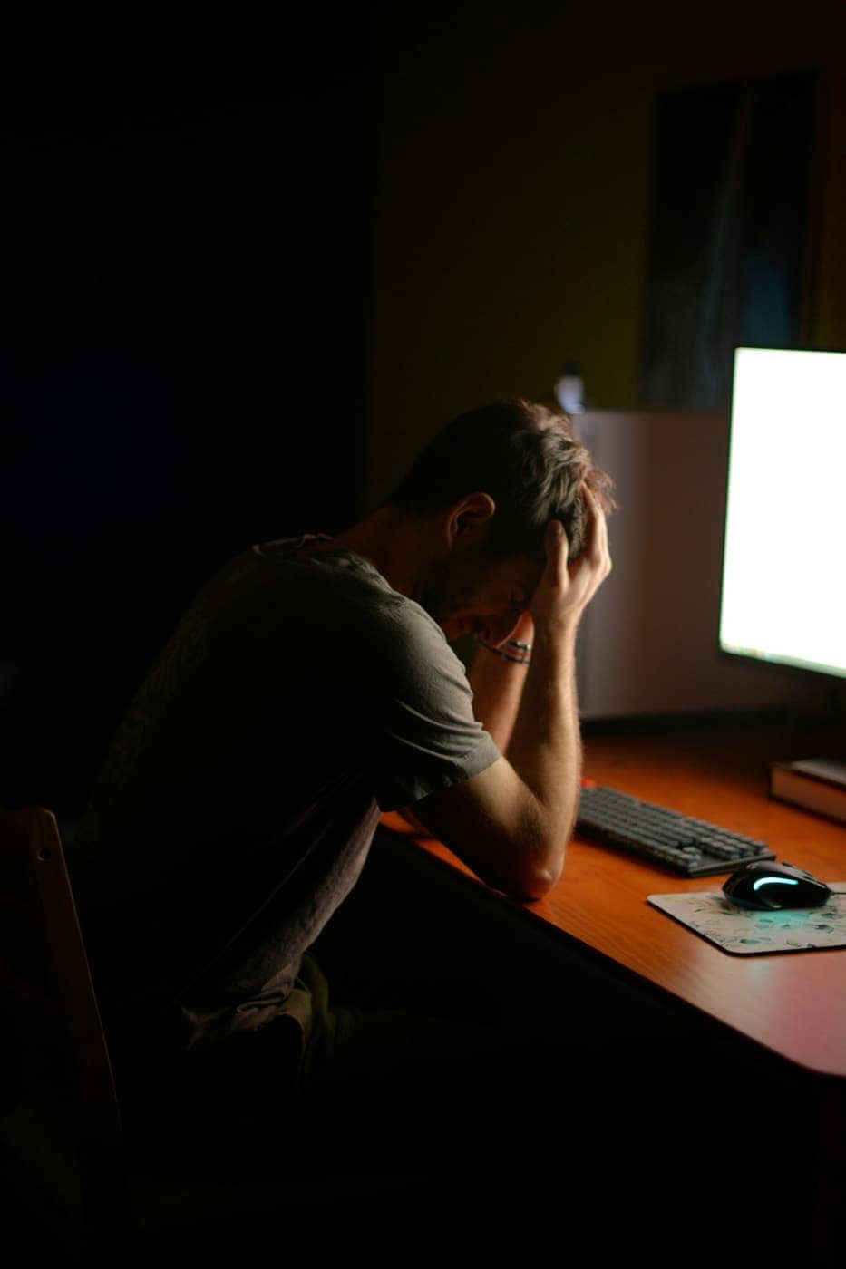 Person at a desk late at night with head in hands beside a bright monitor