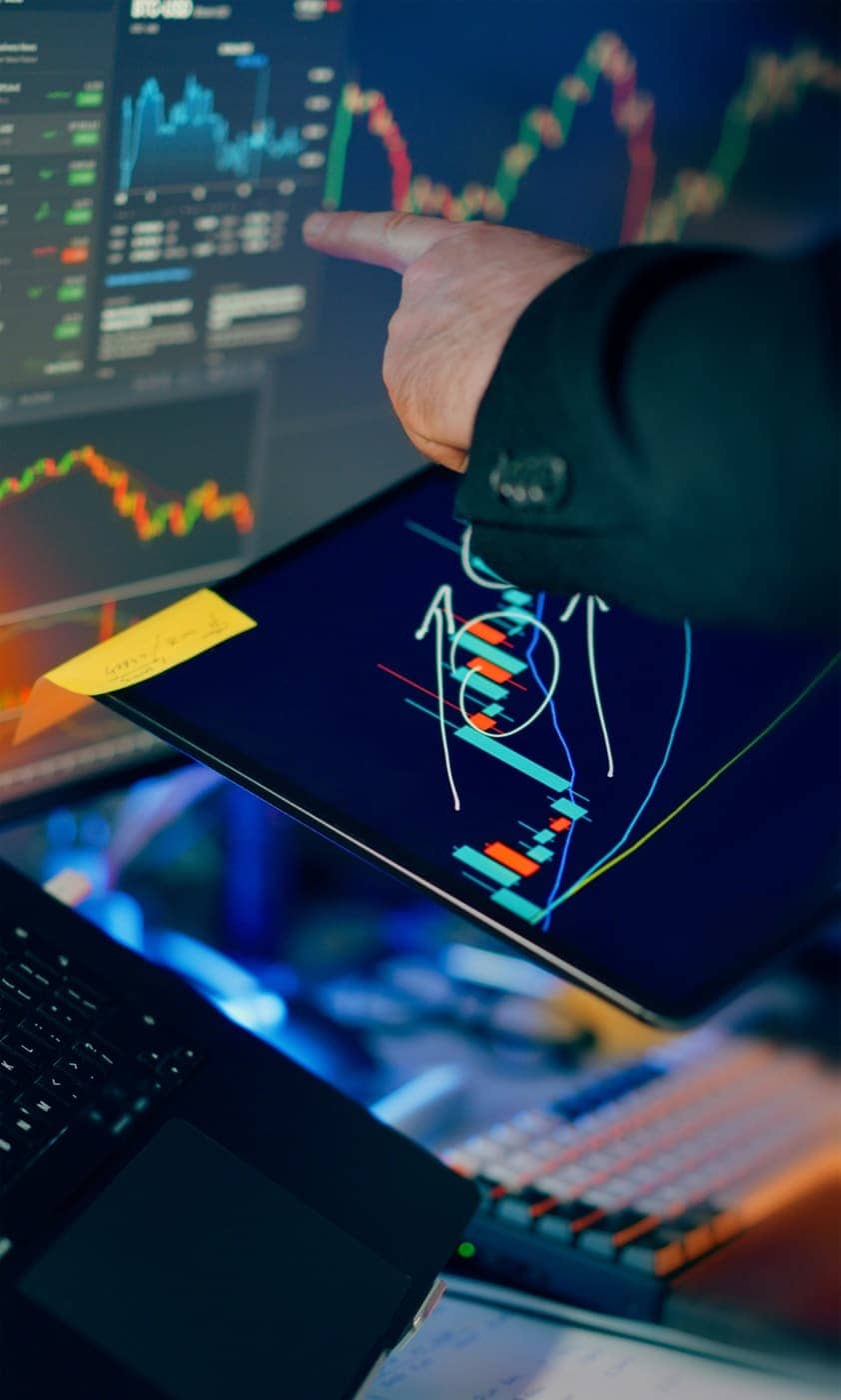 Hand pointing at annotated charts on a tablet and monitors